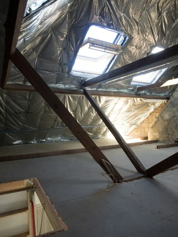 Attic rafters lined with reflective radiant barrier under a skylight