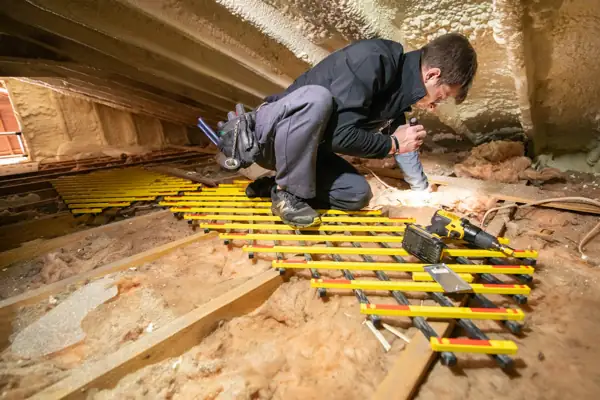 Installer working on an attic floor with tools during insulation work