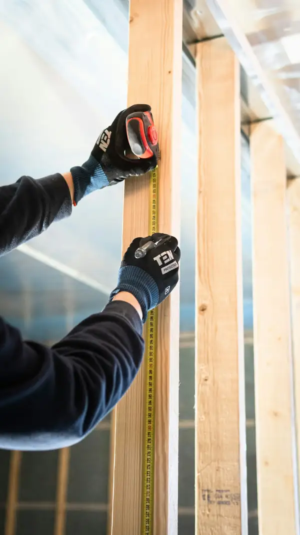 Worker measuring a wall stud before installing insulation