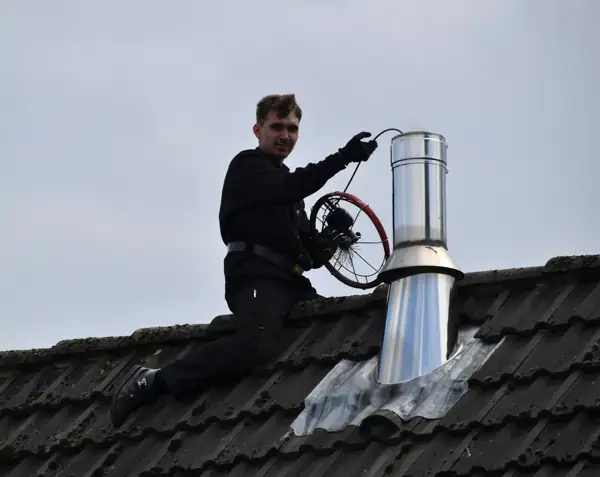 Chimney technician on a roof with a cleaning brush and rods